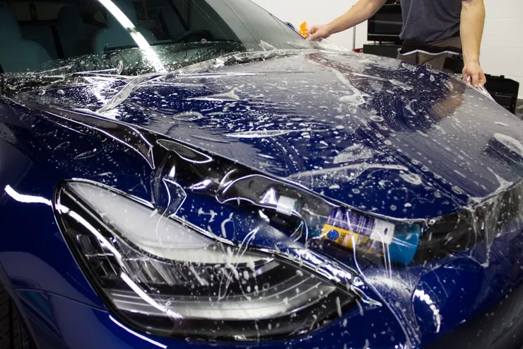 A man is applying protective film to the hood of a blue car.