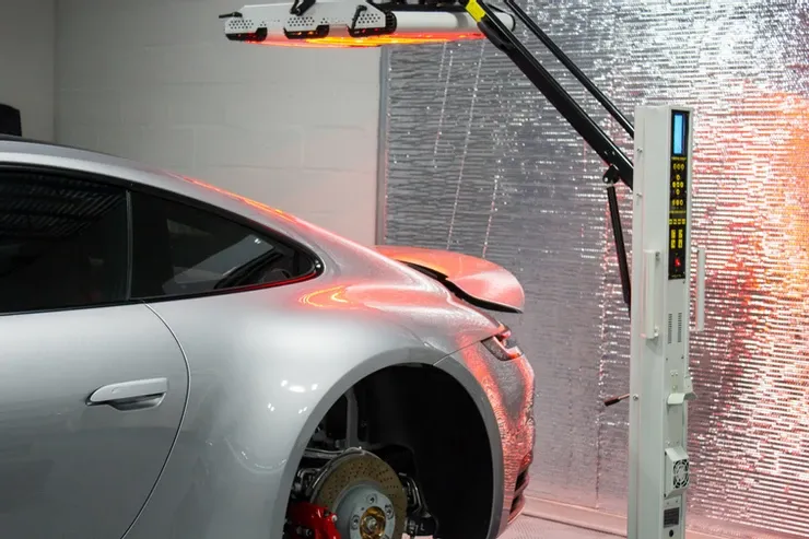 A silver car is sitting under a machine in a garage.