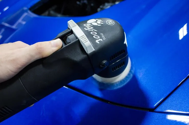 A person is polishing a blue car with a machine.