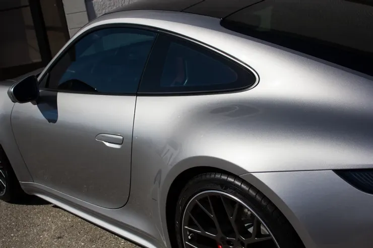 A silver porsche 911 is parked on the side of the road.