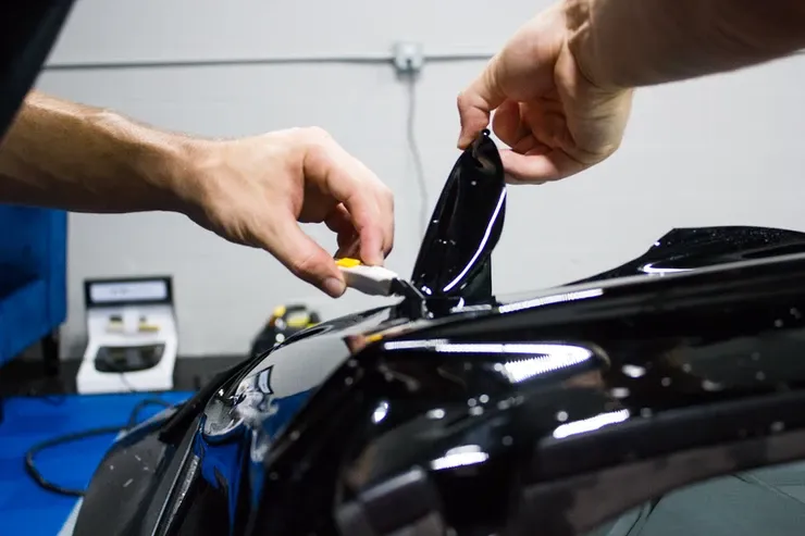 A man is applying tinted film to the roof of a car.