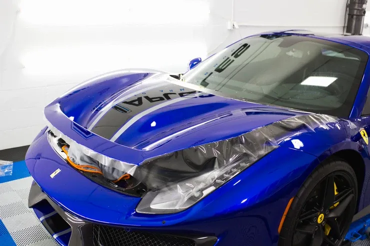 A blue ferrari is wrapped in plastic in a garage.