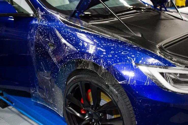 A blue tesla model s is wrapped in plastic and sitting on a lift.