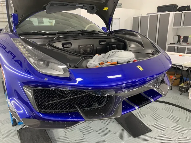 A blue ferrari with the hood up is sitting in a garage.