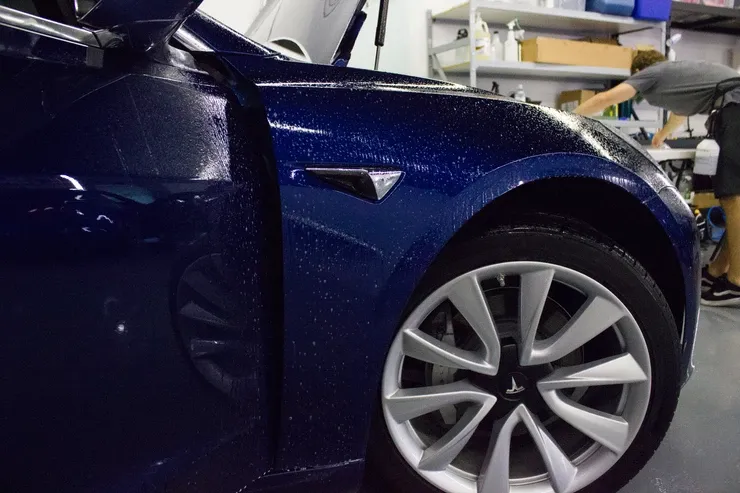 A blue tesla model 3 is parked in a garage.