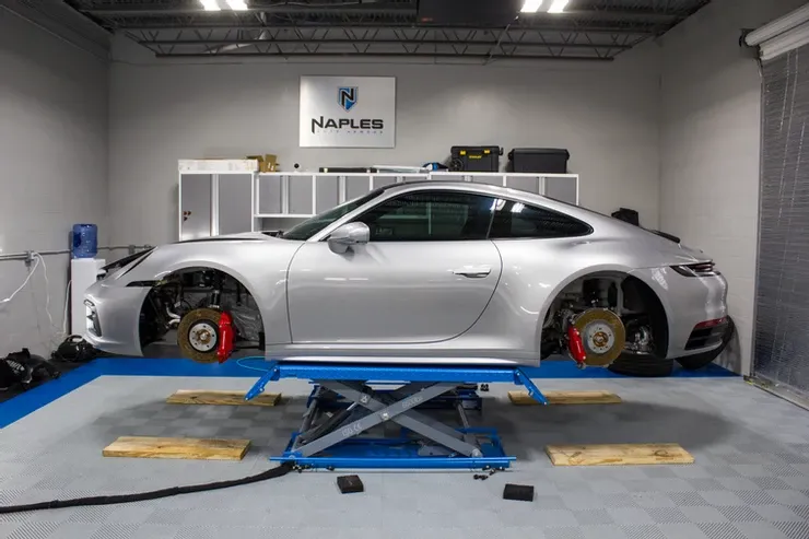 A silver porsche 911 is sitting on a lift in a garage.