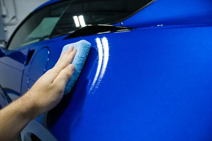 A person is polishing a blue car with a blue cloth.