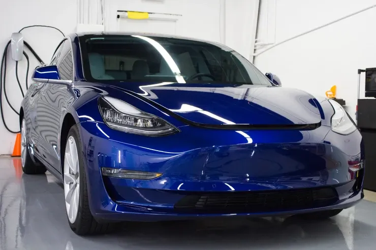 A blue tesla model 3 is parked in a garage.