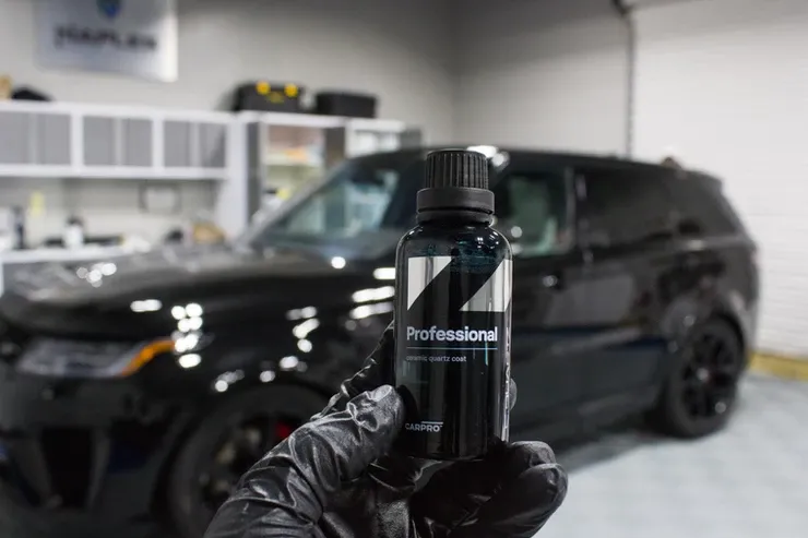 A person is holding a bottle of ceramic coating in front of a black range rover.