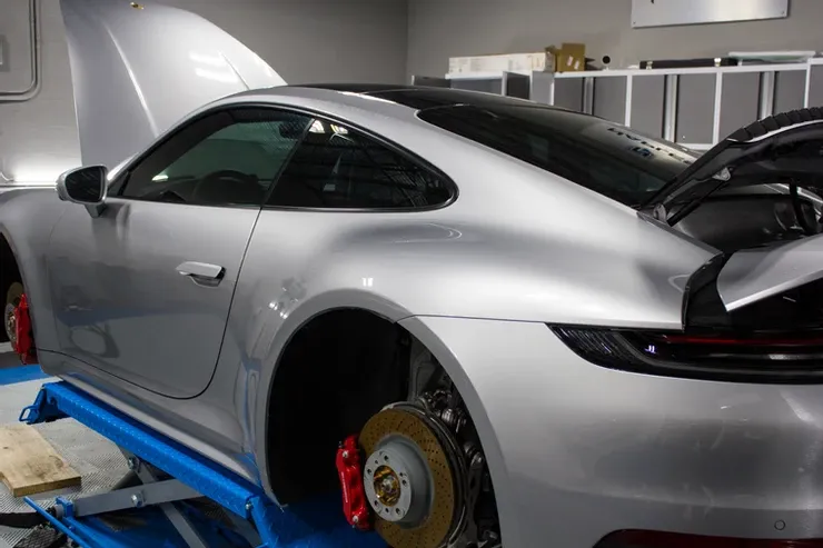 A silver sports car with the hood up is on a lift in a garage.