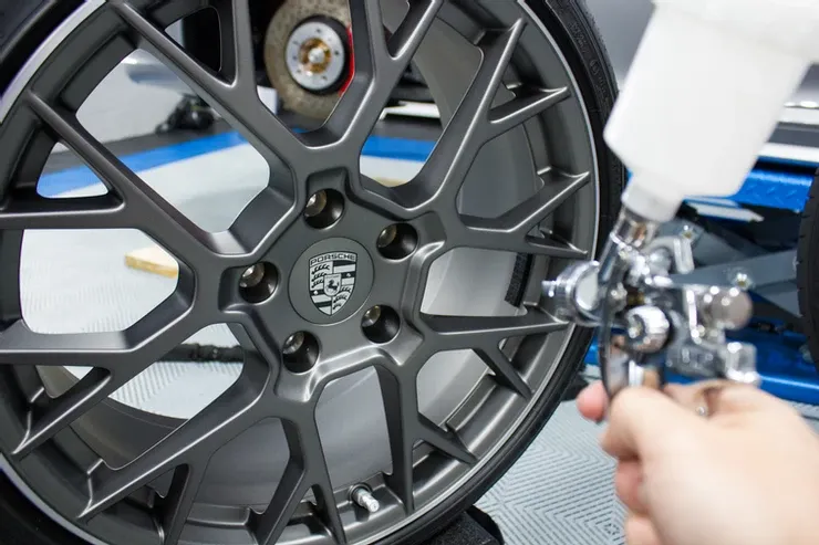 A person is spraying paint on a car wheel with an airbrush.