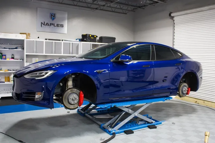 A blue tesla model s is sitting on a lift in a garage.