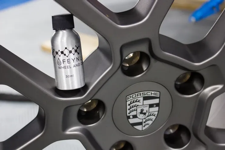 A close up of a porsche wheel with a bottle of feyn wheel cleaner