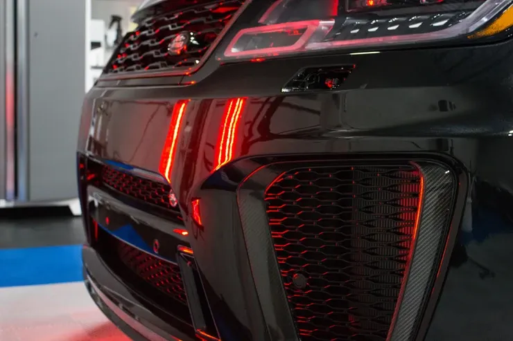 A close up of a black car with red lights on the front bumper.