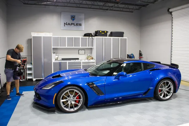 A man is standing next to a blue sports car in a garage.