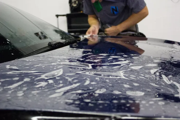 A man is applying a protective film to the hood of a car.