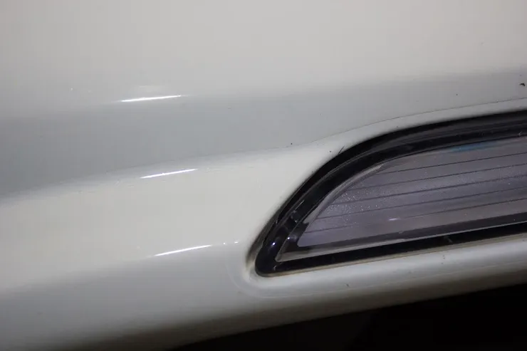 A close up of a white car bumper with a light on it.