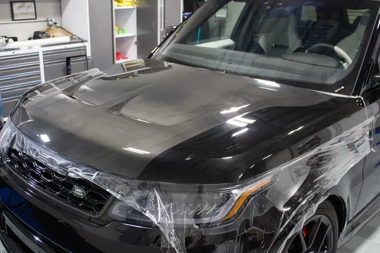 A black range rover is wrapped in plastic in a garage.
