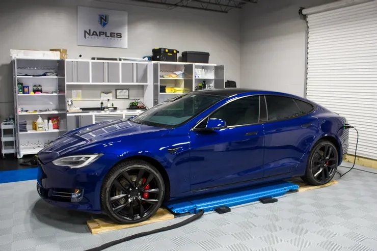 A blue tesla model s is sitting on a lift in a garage.