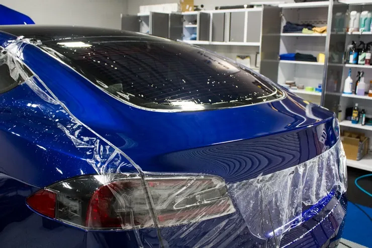 A blue car is wrapped in plastic in a garage.