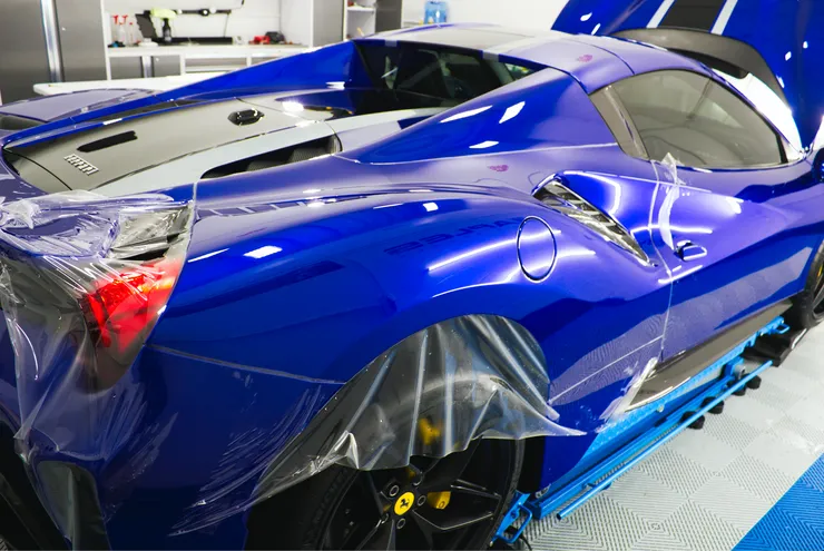 A blue sports car is wrapped in plastic in a garage.
