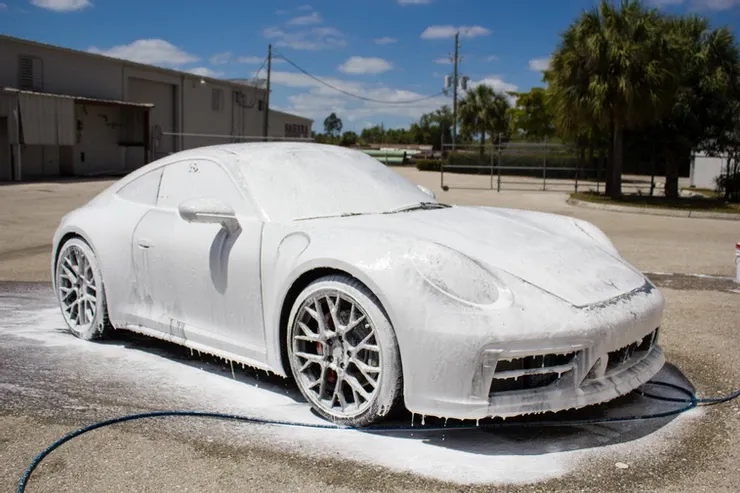 A white car is covered in foam in a parking lot.