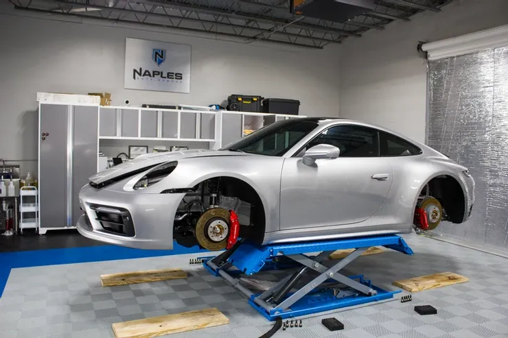A silver porsche 911 is sitting on a lift in a garage.