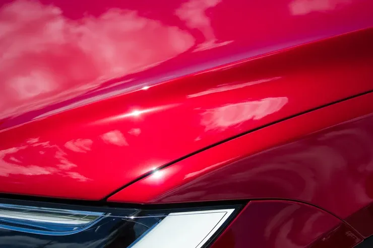 A close up of the hood of a red car with a cloudy sky in the background.