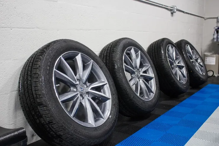 A row of tires are lined up on a blue mat in a garage.