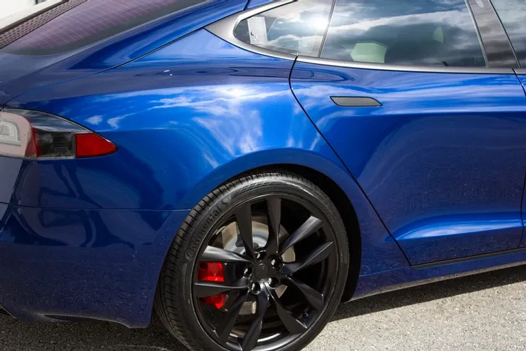 A blue tesla model s is parked on the side of the road.