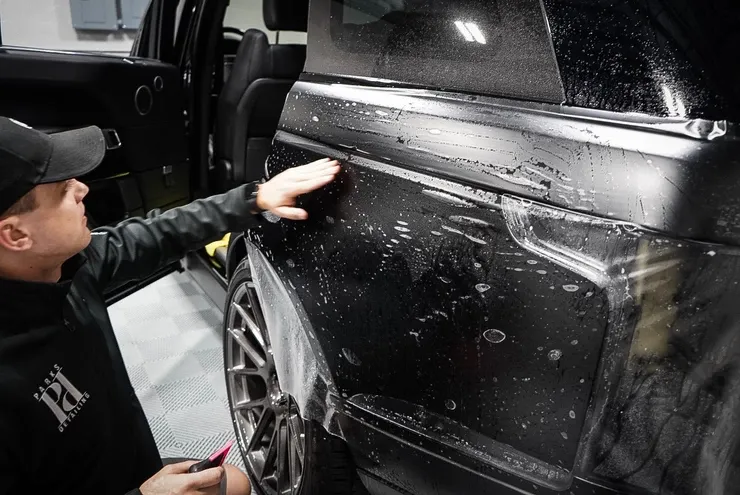 A man is wrapping a black car with a clear film.