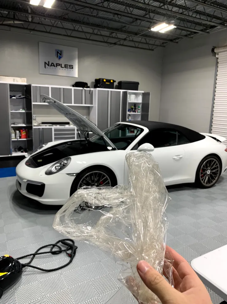 A person is holding a piece of plastic in front of a white sports car.