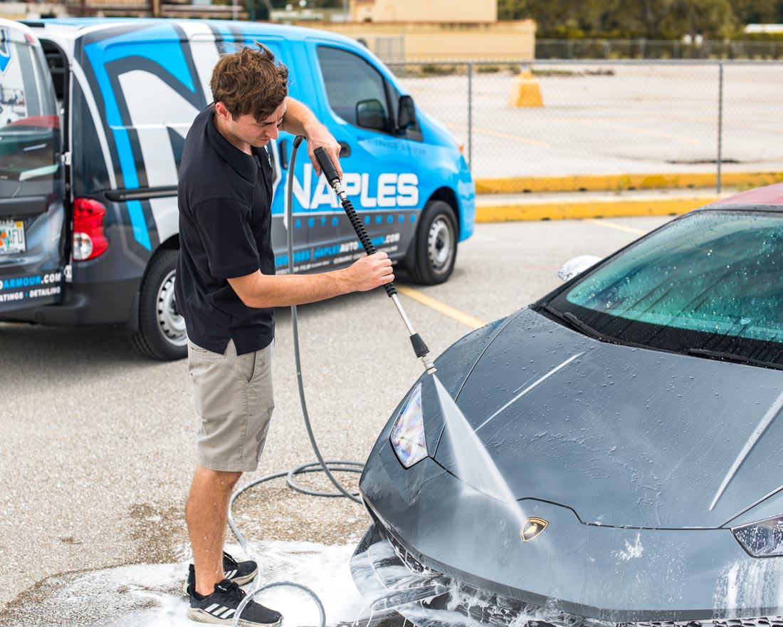 A man is washing a car in front of a van that says naples