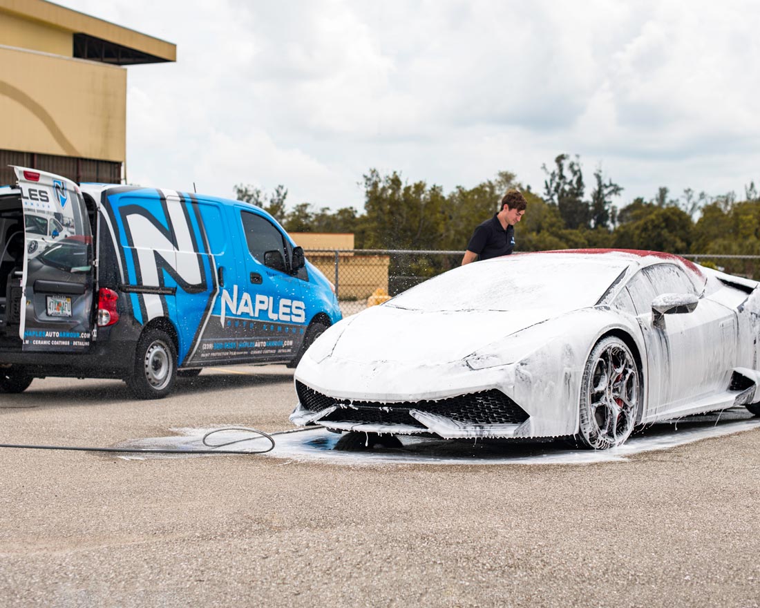 A man is washing a lamborghini with foam next to a van.
