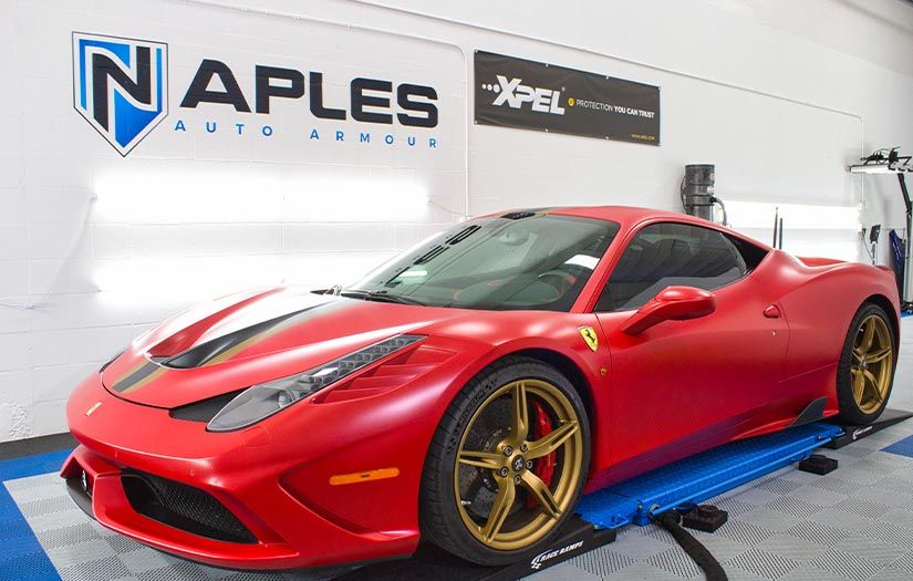 A red ferrari is parked on a ramp in a garage.