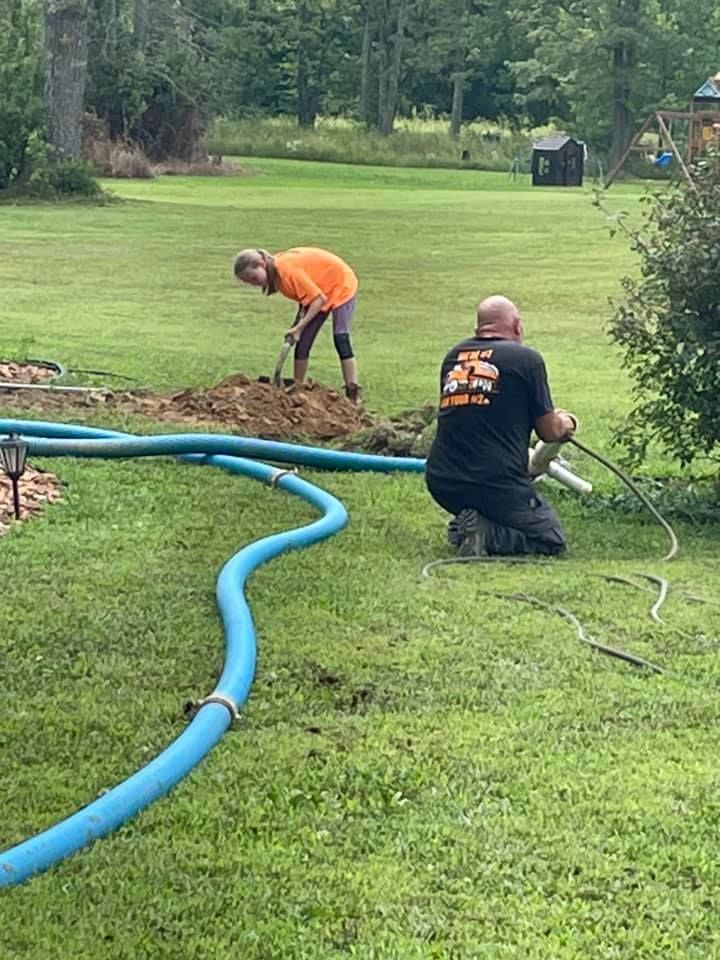 A man and a woman are working in a yard with a hose.