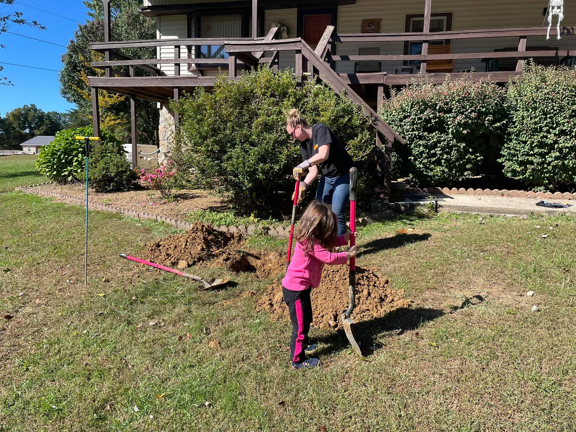 A man and a little girl are digging a hole in the grass in front of a house.