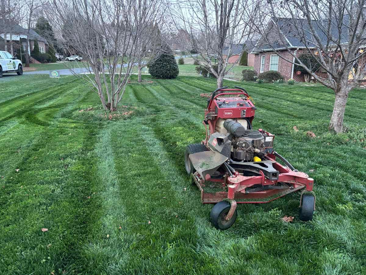 A red commercial lawn mower sits on a freshly cut residential lawn with visible stripes in a suburban neighborhood.