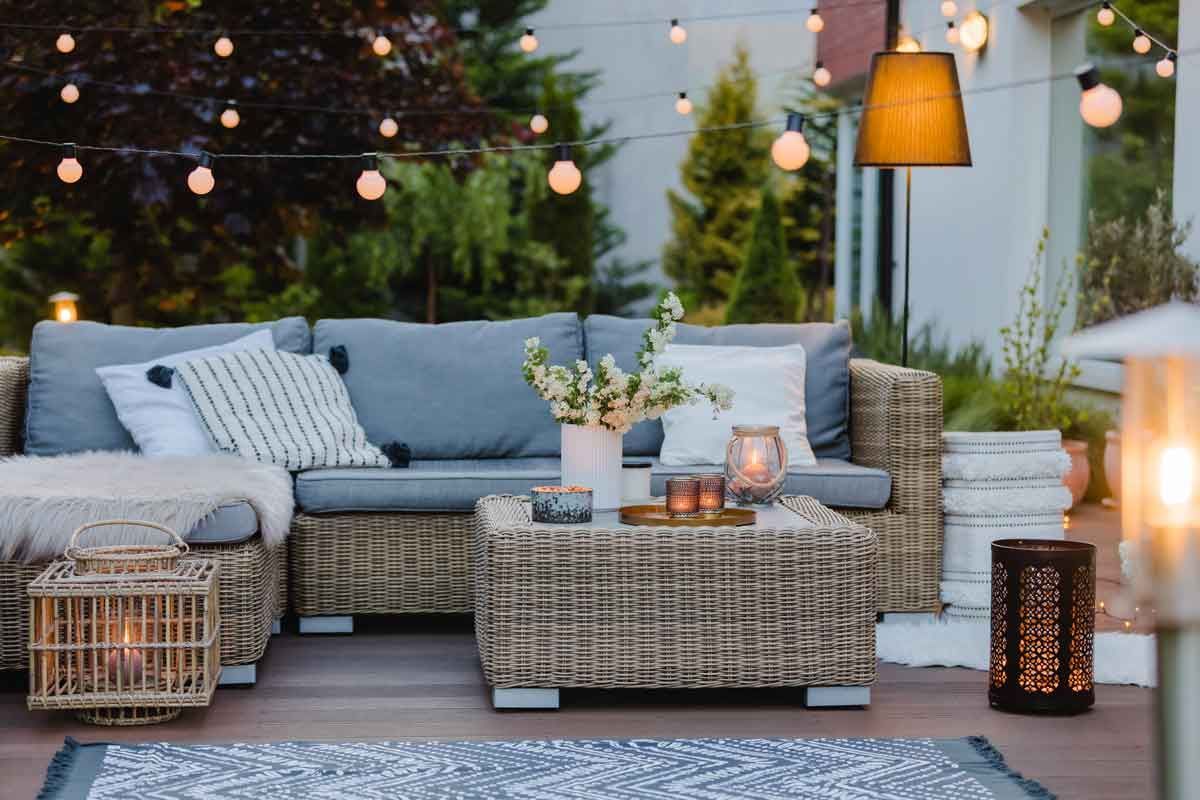 A cozy outdoor patio area with a wicker sectional sofa, a coffee table with candles, and string lights at dusk.