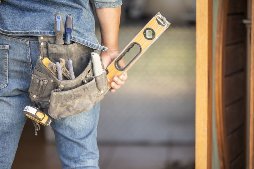 A worker in jeans with a tool belt holding a spirit level.