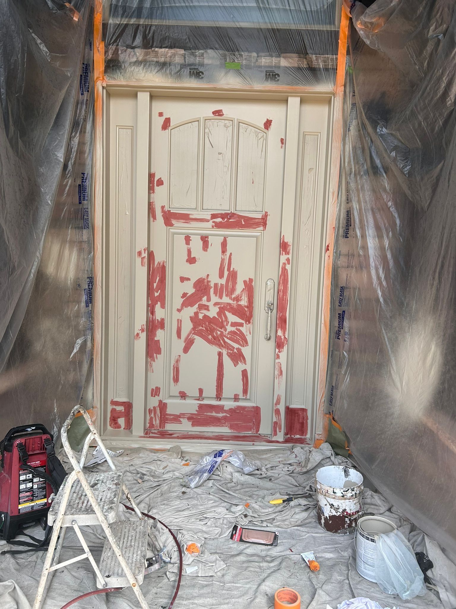 Door being repainted. Old paint peeling, surrounded by plastic sheeting and painting supplies.