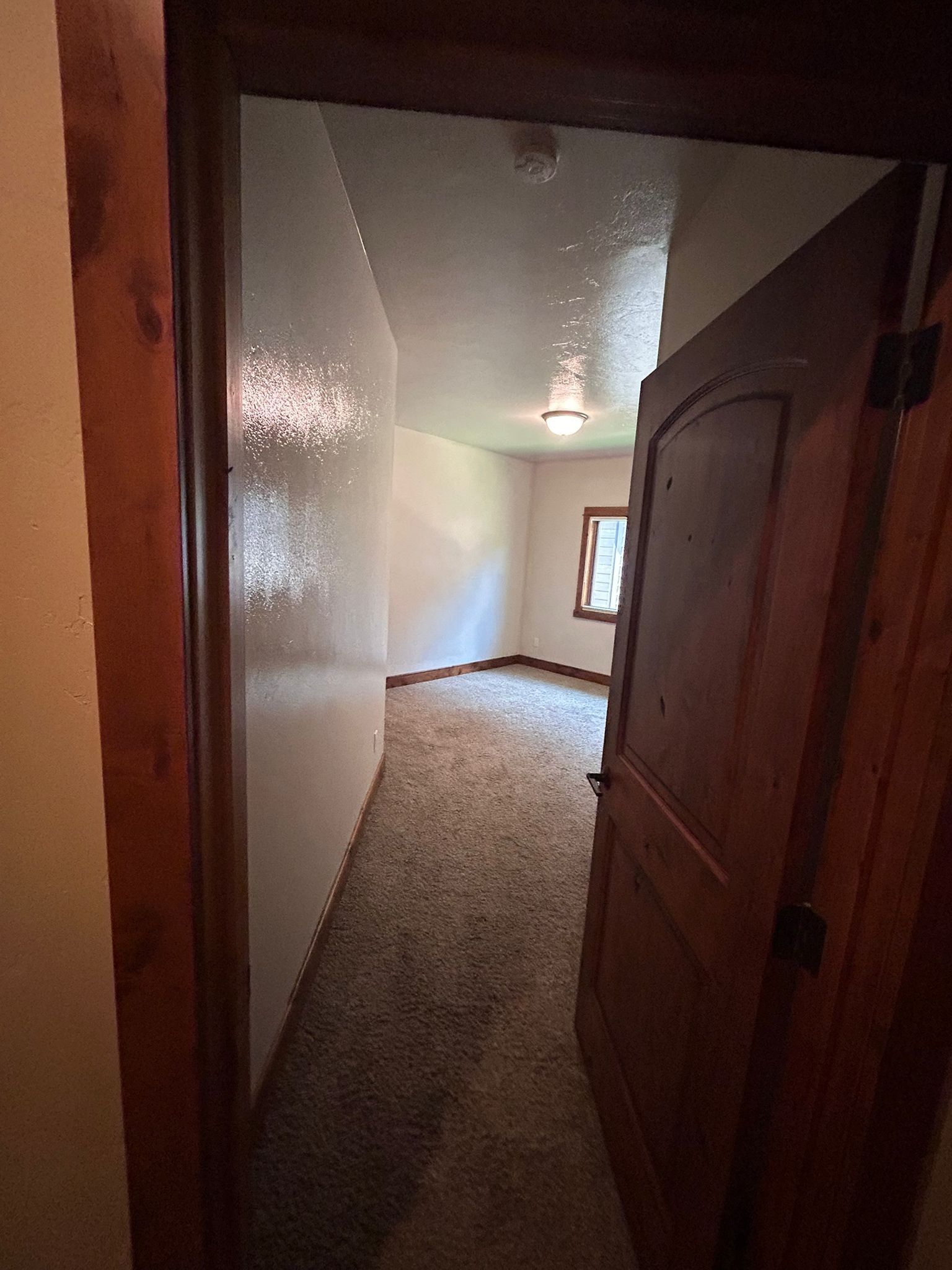 Doorway to a room with white walls, carpet, and a window. Brown door and trim.