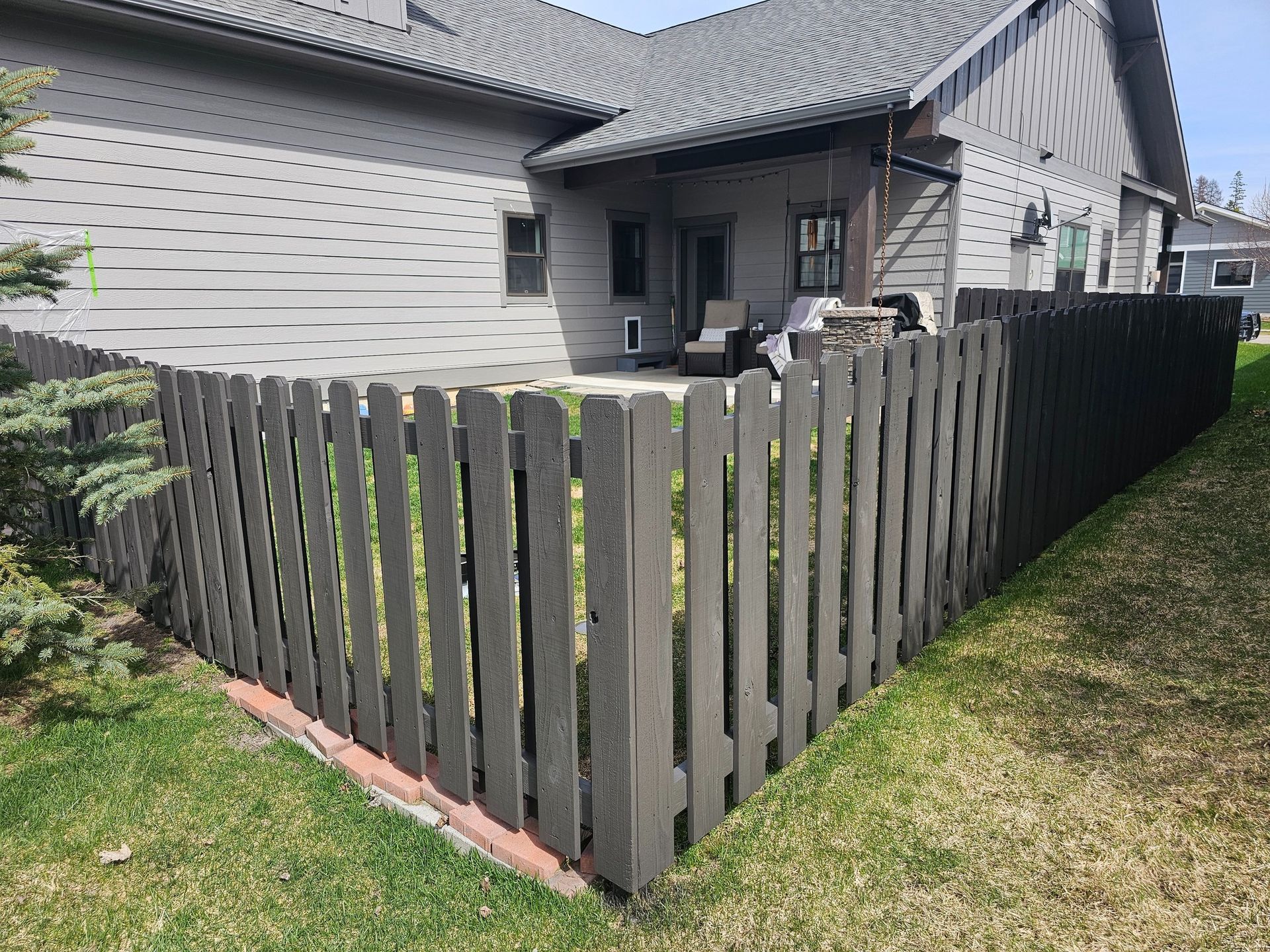 Dark gray picket fence encloses a backyard with a gray house and green grass.
