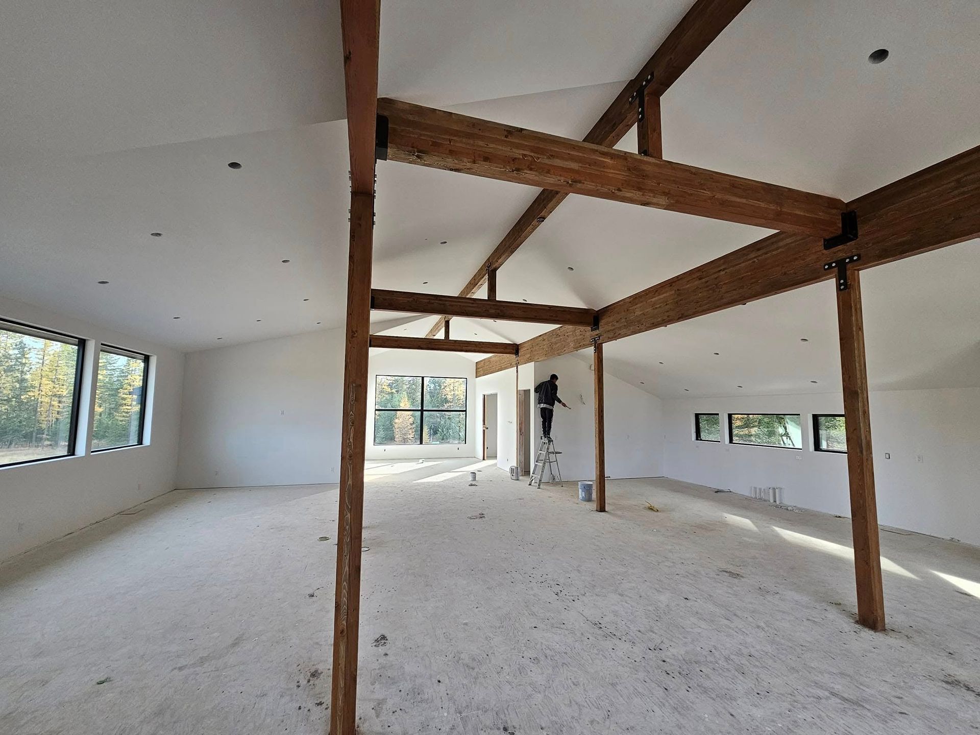 Interior of a building under construction, white walls, exposed wooden beams, and a person on a ladder.