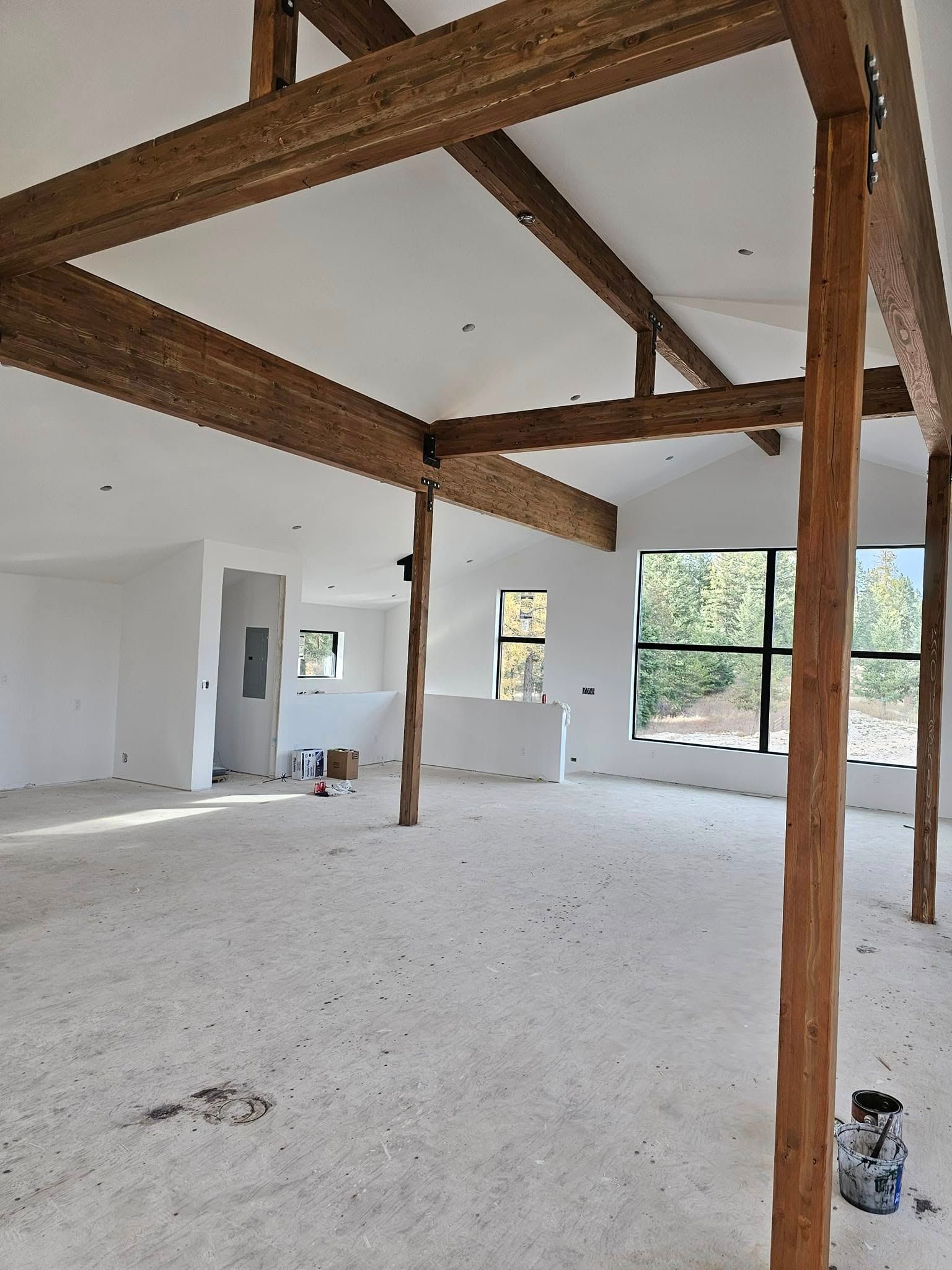 Interior of a house under construction with exposed wooden beams, white walls, and a large window.