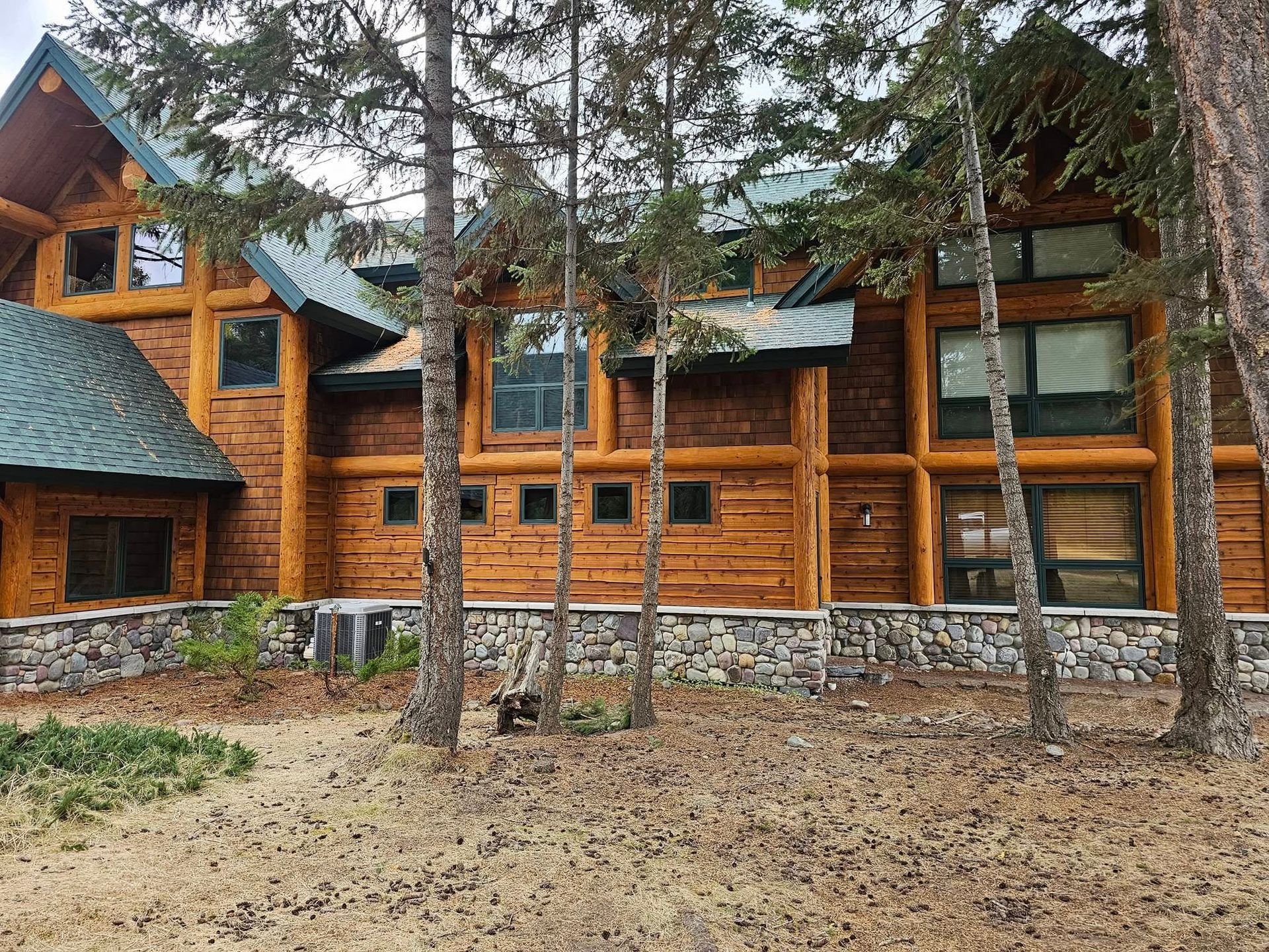 Wooden log cabin house nestled among trees, with stone foundation and green roof.