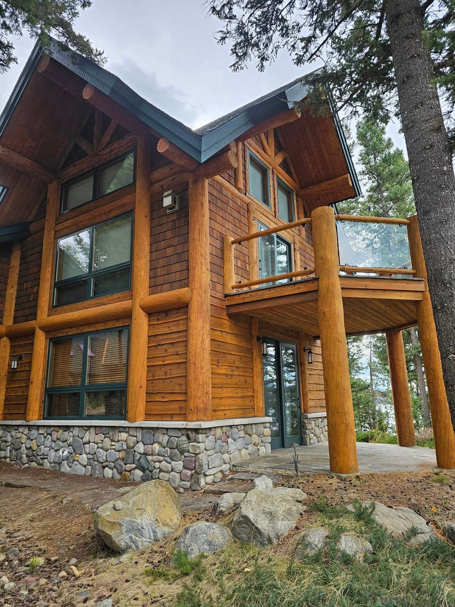 Two-story log cabin with balcony and stone foundation; set among trees and rocks.