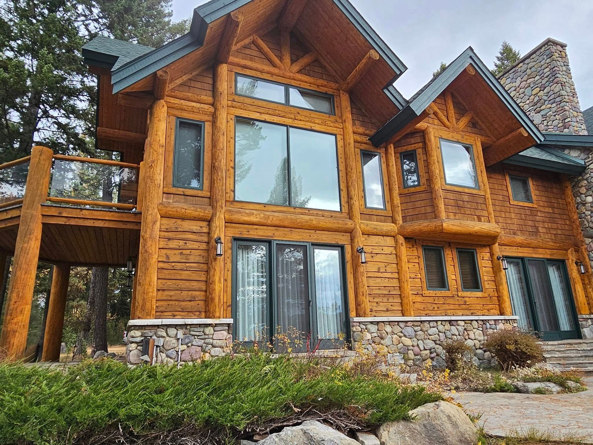 Two-story log cabin with stone accents and a balcony, nestled among trees.