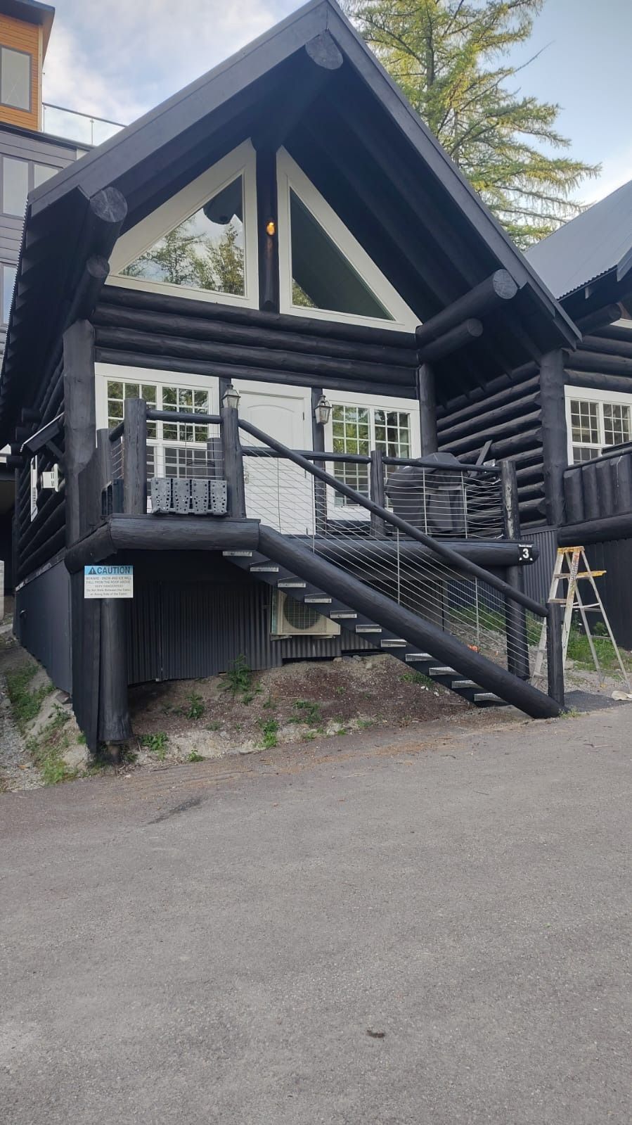 Black log cabin with white-trimmed windows and triangular window above door; stairs lead to small porch.