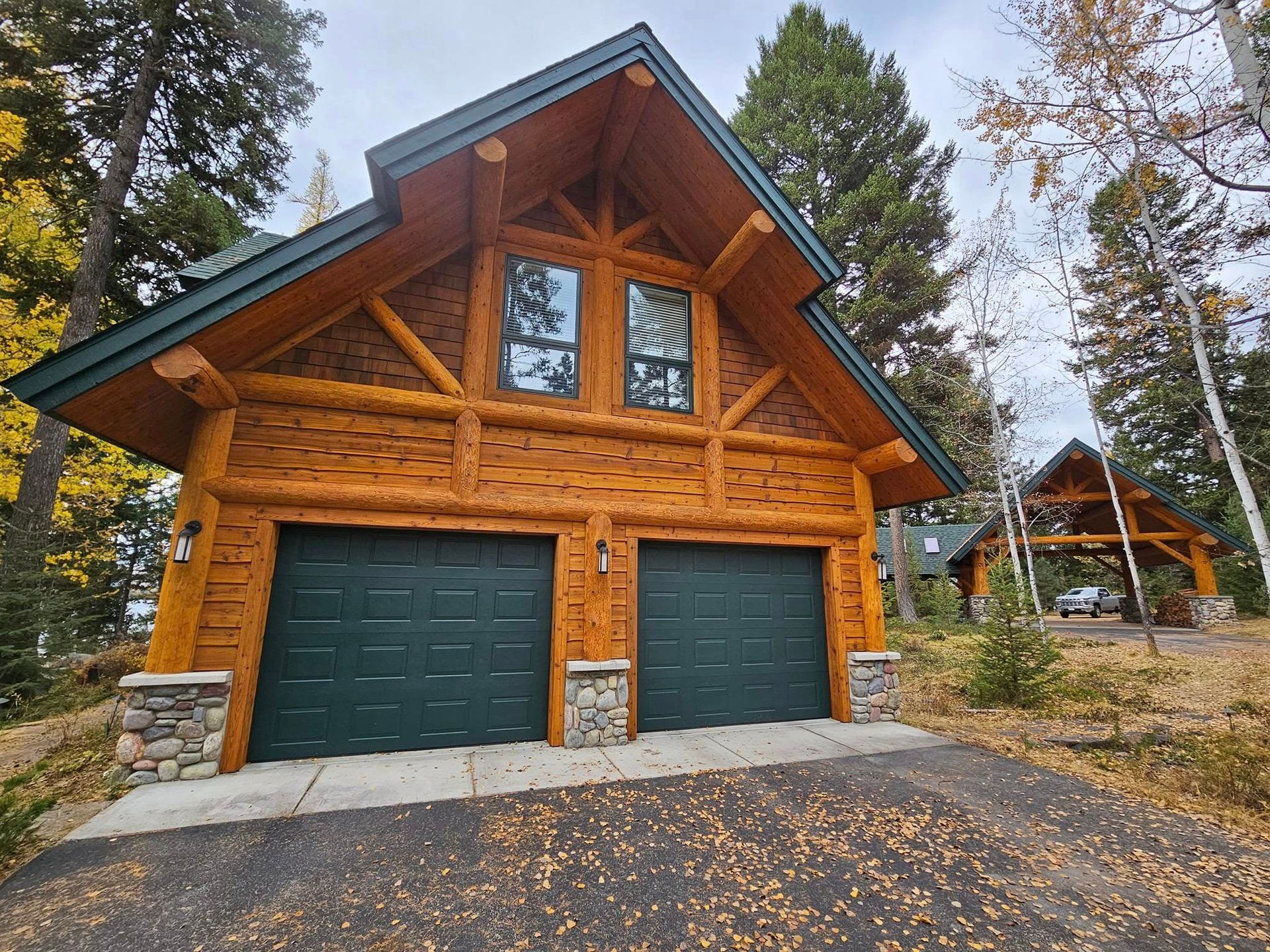 Log cabin with two green garage doors, stone accents, and two upper windows.